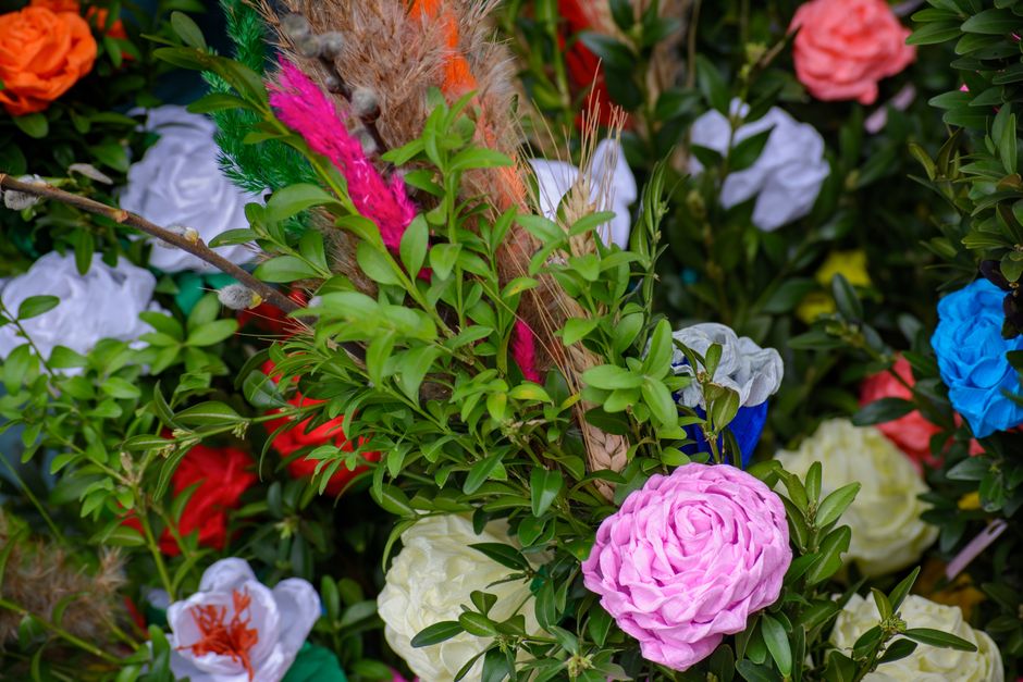 A vibrant floral arrangement featuring a variety of fresh flowers, including a prominent pink ranunculus with layered petals, white roses, and orange lilies. The bouquet is carefully arranged with gre